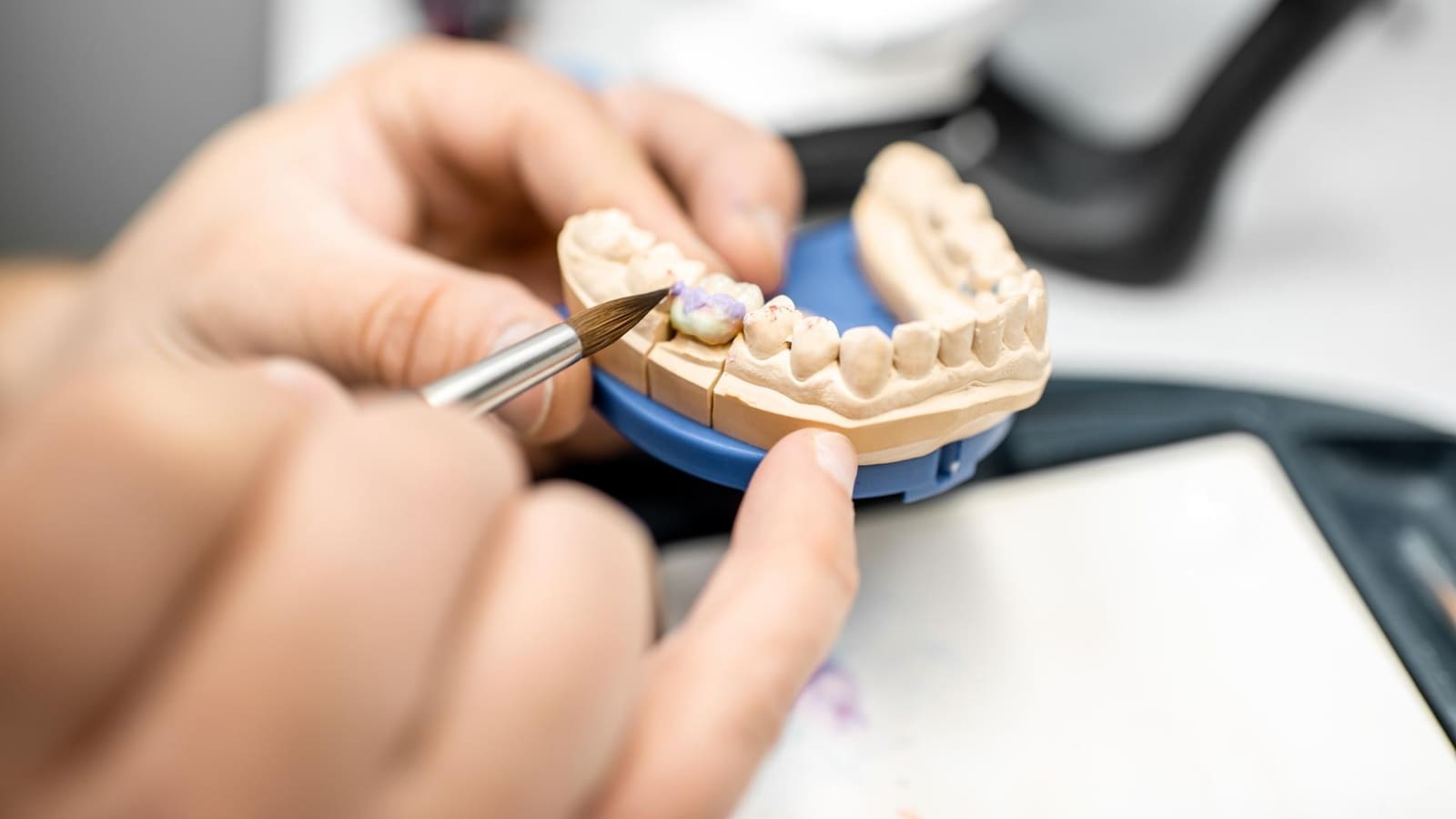 Técnico dental aplicando cerámica con un pincel sobre un modelo de escayola de la dentadura